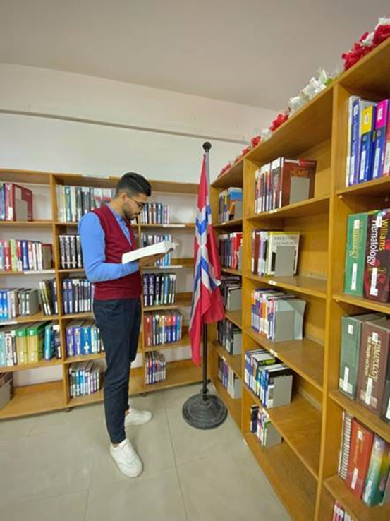 En mann leser i en bok foran noen bokhyller i et bibliotek